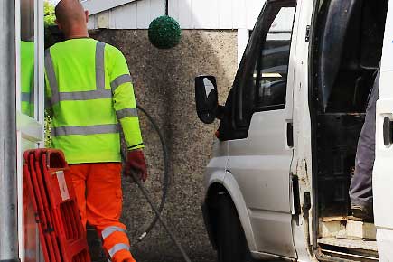 A drains pipes solutions commercial drain jetter in unbranded high visability clothes unloading his plain un-signed van from the side door to clean a business drainage system under contract
