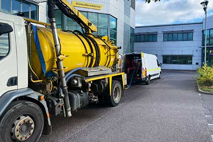 Rear-corner view of our large yellow vacuum truck parked in an industrial estate, ready to carry out contracted drainage clearance and cleaning for business premises.