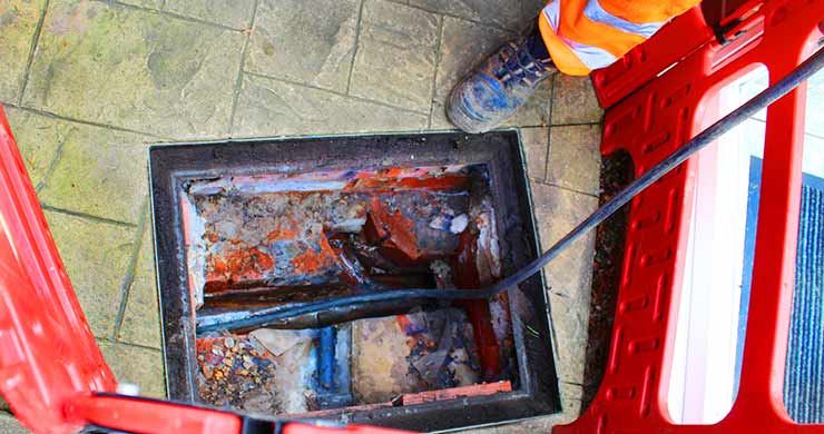 Close-up of one of our drain-jetting and sewer specialists, dressed in yellow and orange hi-vis workwear, with a pipe connected to a spotless three-junction residential drainage system.