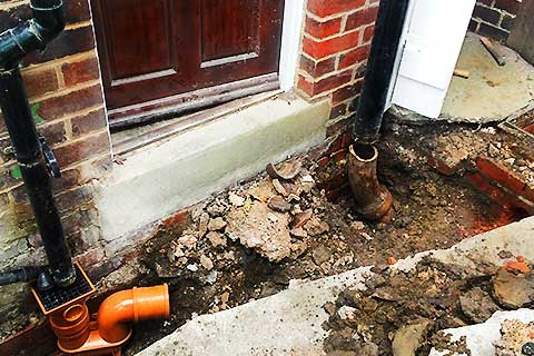 Close view of an excavated rear kitchen yard running parallel to the kitchen step, measuring approximately one and a half metres by one metre, showing the property�s drains and pipes not yet connected and awaiting installation of new drainage