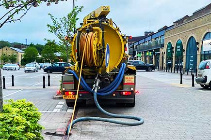 Our specialist jet-vac team clearing a blockage in a Sheffield drain, next to a retail complex with shops and a car park visible.