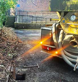 Close-up rear view of a yellow truck with a rear-mounted cylindrical tank reversing into position in front of a raised manhole, ready to carry out vacuum work on drainage at commercial premises in South Sheffield.