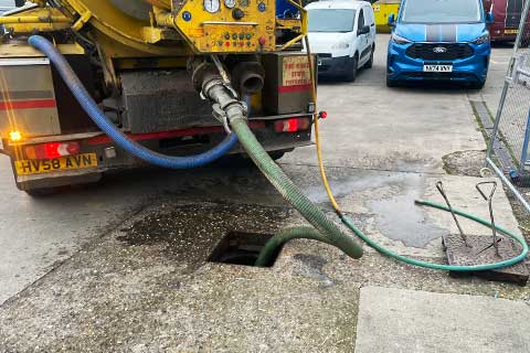 Close-up of the rear of a bright yellow large truck, showing the various controls and meters used to manage and monitor jetting and vacuum settings at the end of a pipe inserted into a retail shop�s drainage system.